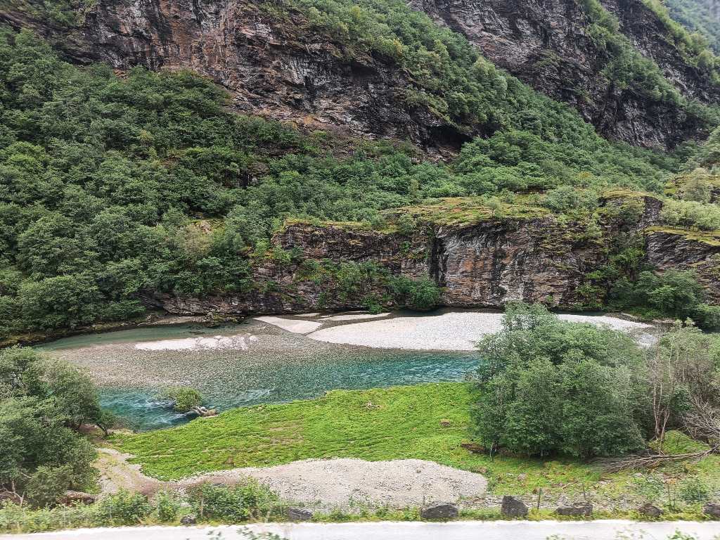 Vista del impresionante paisaje del tren de Flåm con un río de aguas turquesas rodeado de montañas.
