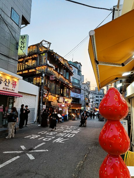 Calle comercial de Seúl con edificios iluminados y una decoración de fresas gigantes en primer plano.