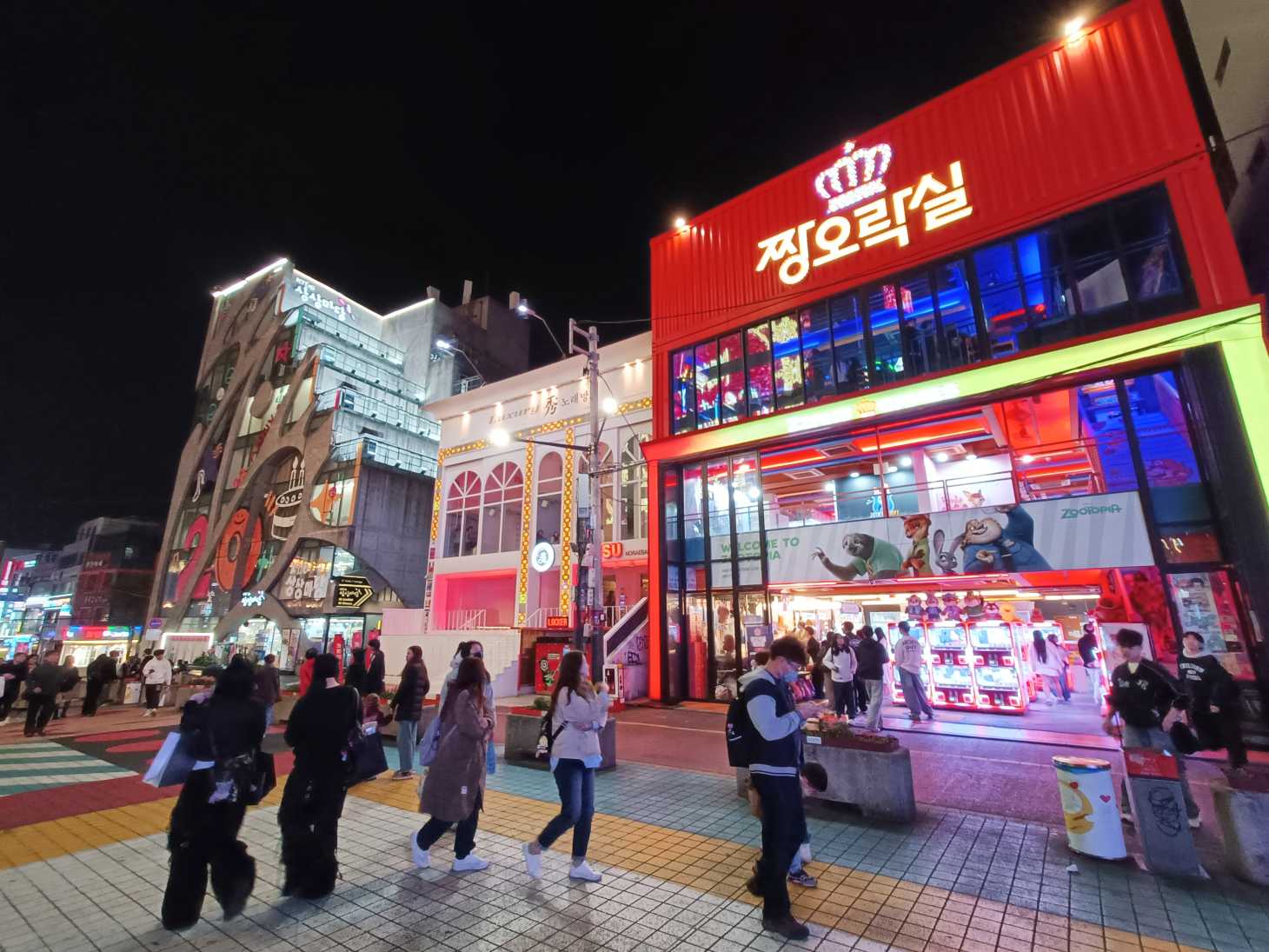 Calle de Hongdae iluminada por la noche, con tiendas, restaurantes y carteles luminosos.